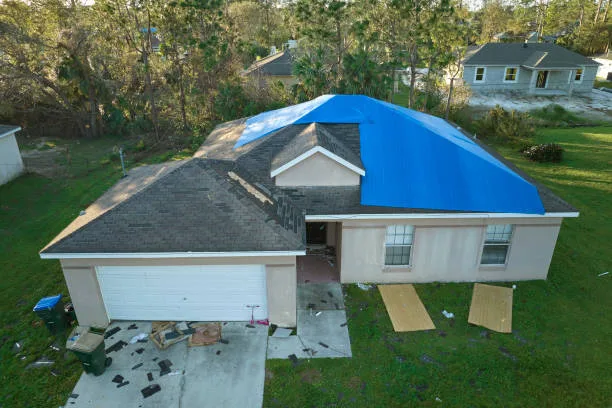 Aerial view of damaged in hurricane Ian house roof covered with blue protective tarp against rain water leaking until replacement of asphalt shingles.