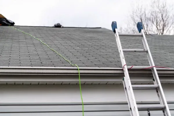 Front closeup of house during day over garage with gray color Single Family Home and roof shingles and ladder during repair