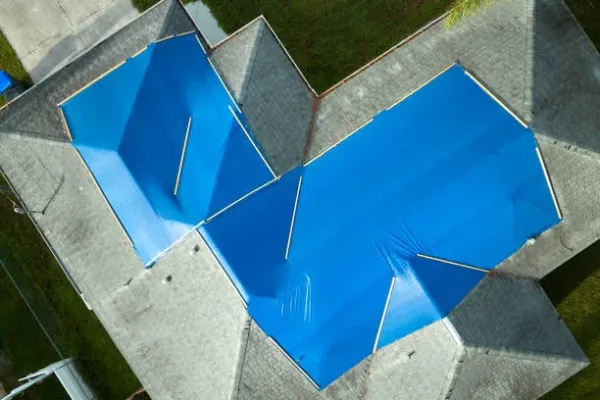 Hurricane Ian damaged house rooftop covered with protective plastic tarp against rain water leaking until replacement of asphalt shingles. Aftermath of natural disaster.