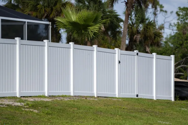 White vinyl picket fence on green lawn surrounding property grounds for backyard protection and privacy.